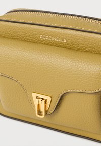 Mala de tiracolo em pele verde-oliva com acabamento texturizado, ferragens em tom dourado, fecho de correr e logótipo da marca estampado na frente.