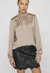 Bluse i lys beige satin med rynket halsudskæring og lange ærmer; parret med en sort blonde nederdel med intrikate blomster mønstre.