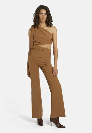 Bruin tweedelig outfit met een top met één schouder en ruches en hoge, uitlopende broek. Gekozen met bruine hoge laarzen.