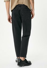 Jeans de mezclilla negra con un corte recto, textura desgastada, bolsillos traseros estándar y una cintura alta, combinados con zapatos de vestir negros.