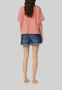 T-shirt en coton rose à manches courtes, associé à un short en jean avec un ourlet retroussé et des poches arrière. Le modèle porte des sandales à lanières beiges.
