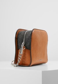 Brun lædertaske med vævet tekstur, gråt ulddetalje, sølvfarvet lynlås og kædestrop. Firkantet form, robust konstruktion, minimal branding.