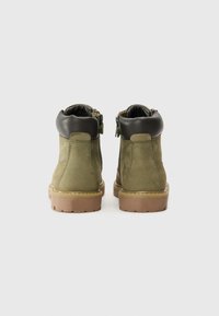 Bottines en daim vert avec une manche en cuir marron, fermeture éclair latérale et semelle en caoutchouc. Coutures détaillées sur le dessus et finition texturée.