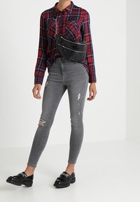 Camisa de cuadros roja y azul de manga larga combinada con unos pantalones ajustados grises desgastados y unos mocasines negros de imitación piel, con un bolso bandolera texturizado negro.