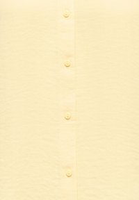 Ανοιχτό κίτρινο πουκάμισο με κουμπιά, κατασκευασμένο από υφή υφάσματος με εμπρόσθιο καπάκι που διαθέτει κουμπιά τοποθετημένα ομοιόμορφα.