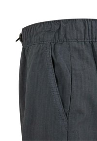 Närbild av mörkgrå byxor med elastisk midja, sidoficka och subtil rutstruktur på tyget.