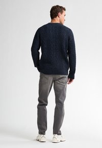 Pulover tricotat bleumarin cu model cu cabluri, manșete și tiv cu nervuri, asortat cu blugi gri din denim și adidași albi. Siluetă structurată.