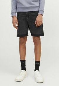 Shorts en jean noir avec des revers, portés avec des baskets blanches et des chaussettes noires. Le haut est un sweat-shirt gris clair.
