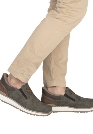 Chaussures à enfiler marron et grises avec une tige en cuir, des panneaux élastiques latéraux et une semelle blanche texturée, portées avec un pantalon beige.