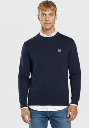 Suéter azul marino hecho de material de punto, con un escote redondo, puños acanalados y un pequeño logo bordado en el lado izquierdo del pecho.