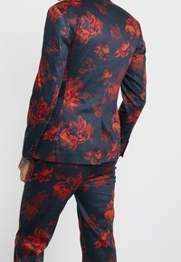 Completo navy con motivo floreale rosso, realizzato in un tessuto con leggero lucido. Caratterizzato da una vestibilità su misura, rever connotati e due spacchi posteriori.