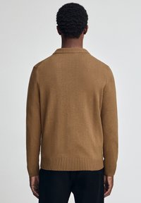 Brązowy sweter dzianinowy z miękkiego materiału. Posiada ściągacze u dołu i przy mankietach, okrągły dekolt oraz bezszwowy krój w okolicy ramion.