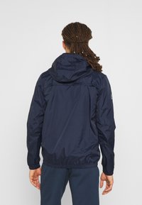 Mörkblå lättviktsjacka med huva, elastiska ärmar och åtdragen midja. Slät, glansig textur med minimal synlig detaljer.