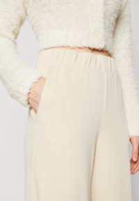 Crèmekleurige, textuurgekropte trui met een fuzzy afwerking en een knoopdetail, gecombineerd met beige, elastische taille, wijde broekspijpen met zijzakken.