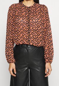 Blus med långa ärmar, i en rosa och svart abstrakt tryck. Tillverkad av lätt material, med en lätt lyster och knäppning framtill.