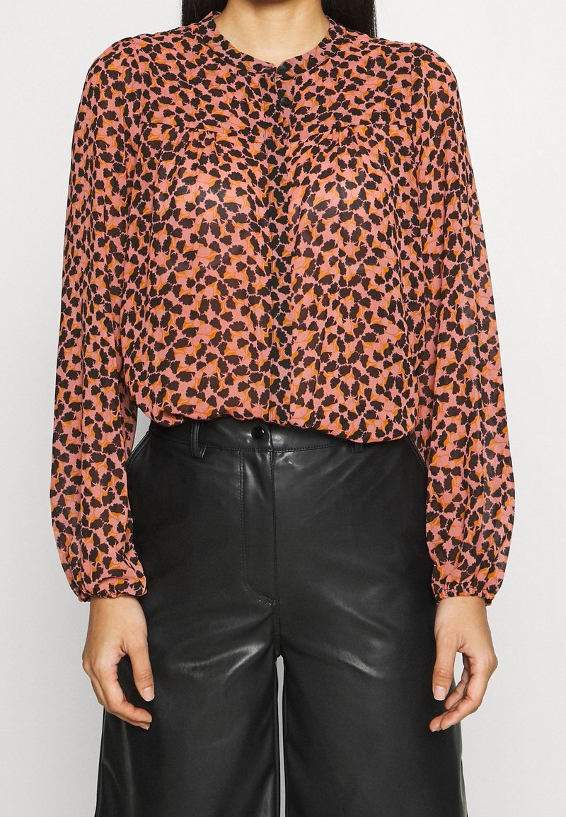 Blus med långa ärmar, i en rosa och svart abstrakt tryck. Tillverkad av lätt material, med en lätt lyster och knäppning framtill.