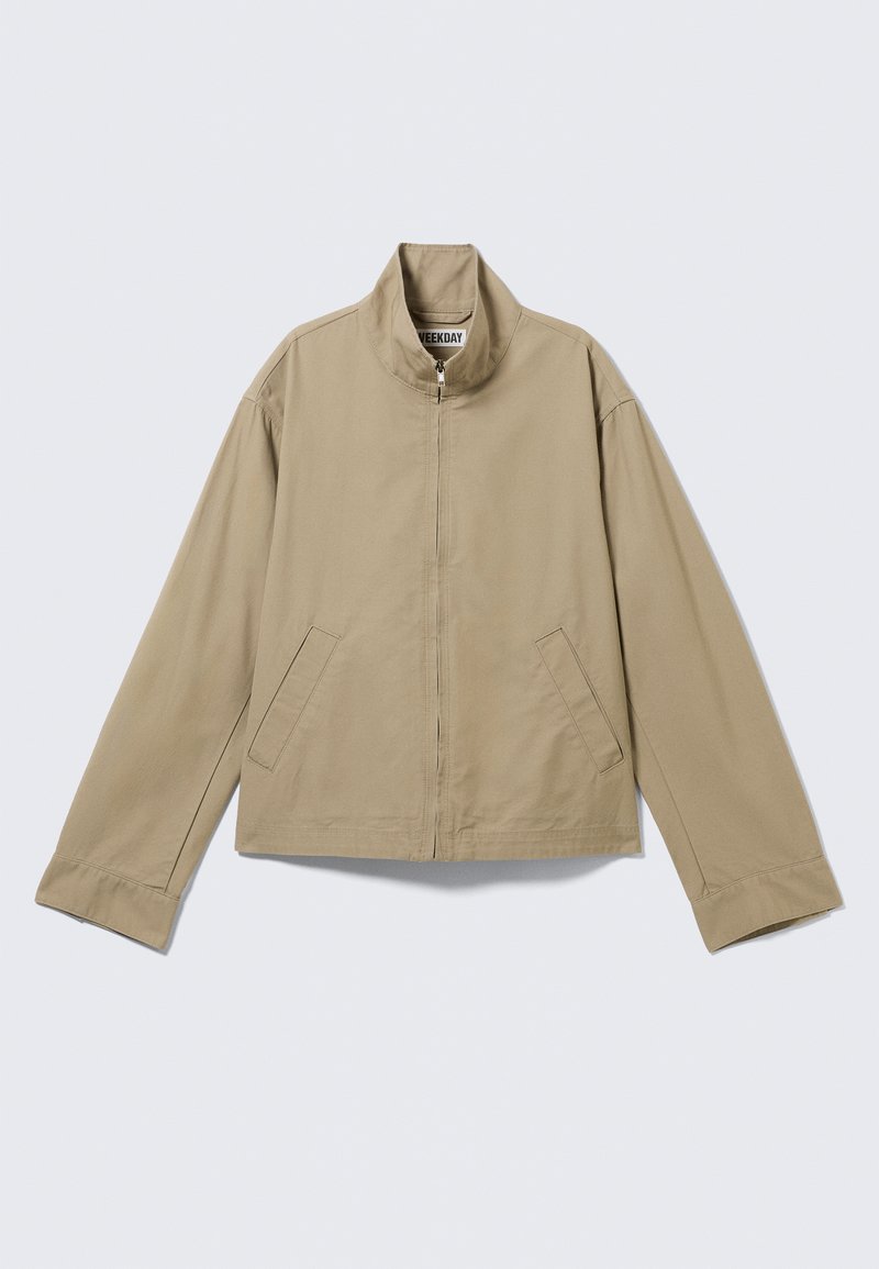 Veste beige zippée avec col montant, manches longues et deux poches latérales, étalée à plat sur un fond clair.
