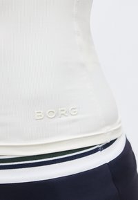 Κοντινό πλάνο λευκού ριγωτού τοπ με την εγχάρακτη λέξη "BORG" κοντά στο τελείωμα, συνδυασμένο με παντελόνι με ναυτικό και λευκό ριγέ λάστιχο στη μέση.