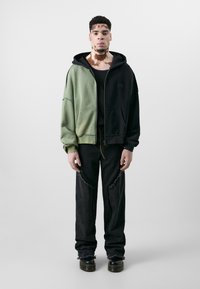Hoodie features green and black color-blocking, zip closure, and oversized design. Worn with distressed black jeans and platform boots.