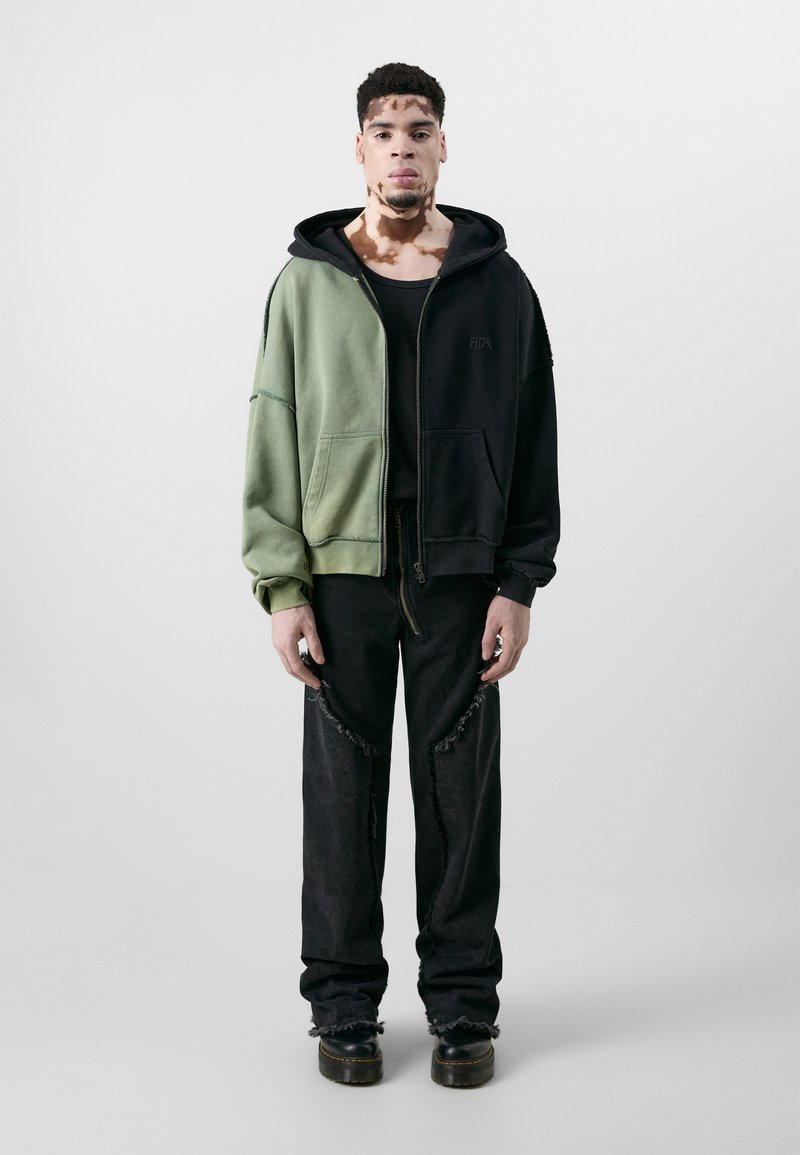 Hoodie features green and black color-blocking, zip closure, and oversized design. Worn with distressed black jeans and platform boots.