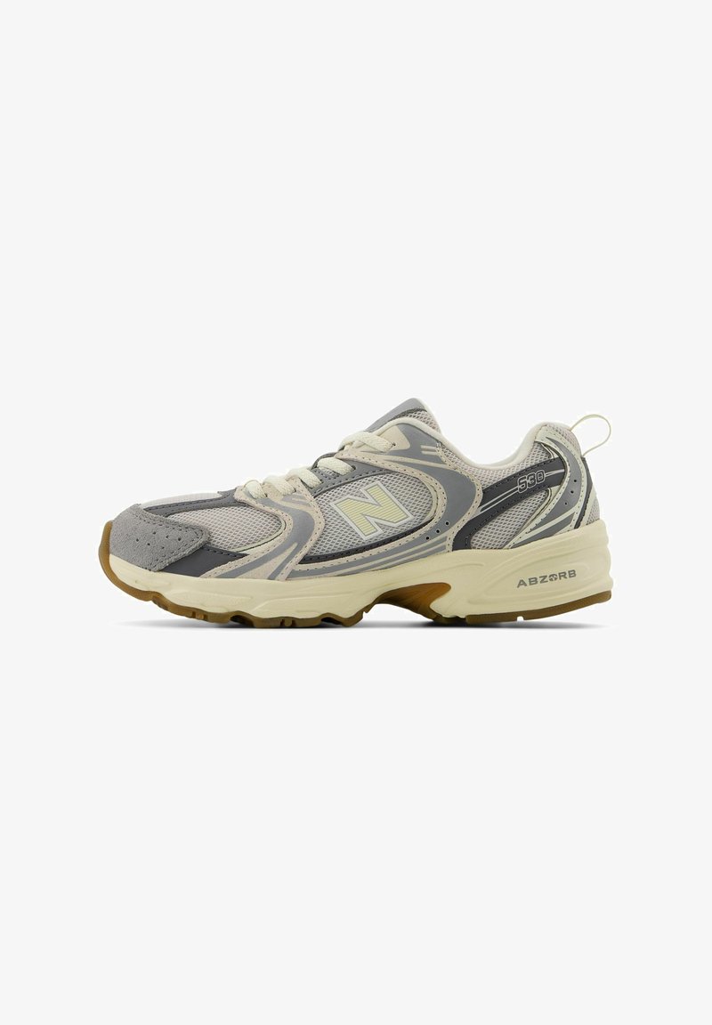 Zapatilla deportiva en gris y crema con parte superior de malla, cuello acolchado, suela de goma y el logo "ABZORB" en el lateral. Incluye cordones y tirador.