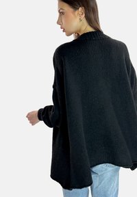 Suéter negro de gran tamaño con tejido texturizado, mangas anchas, cuello acanalado y dobladillo curvo, combinado con vaqueros de mezclilla azul claro.