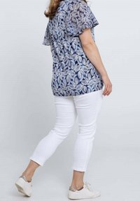 Blauw-witte blouse met bladmotief gecombineerd met witte slanke broek en lichte sneakers, die een casual outfitstijl laten zien.