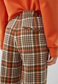 Geruite broeken in tinten bruin, oranje en wit hebben een hoge taille, zijzakken en een gladde, gestructureerde stofafwerking.