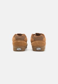 Brązowe zamszowe trampki Vans o zaokrąglonym kształcie, z wyściełanym kołnierzem i detalami logo na pięcie. Gumowe podeszwy z charakterystycznym oznaczeniem.