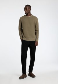 Khaķi adīta džemperis ar teksturētu apdari, kombinēts ar melnajām biksēm un brūnajām potīšu zābakiem. Vienkāršs apaļš kakla izgriezums un ribotas aproces.