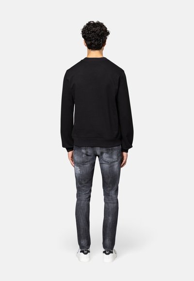 Zwarte sweatshirt met een geribbelde onderrand en mouwen, gecombineerd met vervaagde grijze jeans met versleten details, en witte sneakers met een subtiel logo.