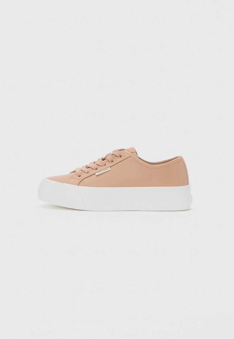 Low-top pastel pink sneaker with lace-up front, white platform sole, and small metallic logo tag on side.