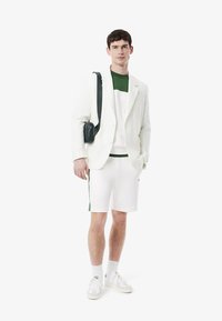 Blazer blanco sobre una camisa de bloques de color verde y blanco, combinado con pantalones cortos blancos. Los accesorios incluyen un pequeño bolso cruzado negro. Zapatillas blancas.