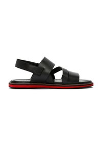 Zwarte leren sandalen met kruissluiting, een gevoerd voetbed en een zool met rode accenten. Open achterkant voor gemakkelijk aan- en uittrekken.