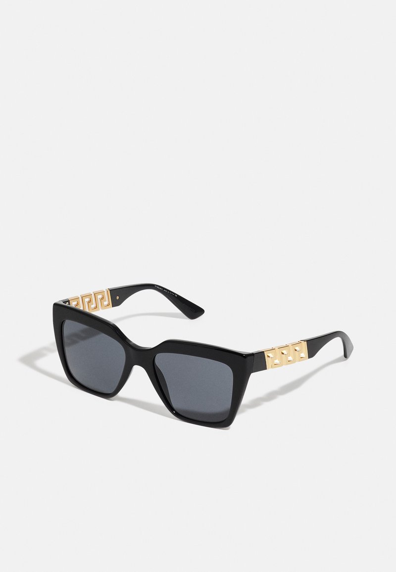 Óculos de sol pretos com armação quadrada, lentes cinza com tonalidade e detalhes geométricos dourados nas hastes. Material plástico suave.