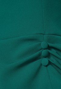 Tissu teal avec trois boutons recouverts et un détail froncé le long d'une couture verticale.