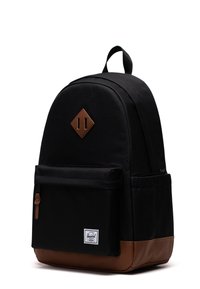 Zaino in tessuto nero con parte superiore arrotondata, dettagli in pelle marrone, tasca frontale e un patch a forma di diamante con due strisce verticali.