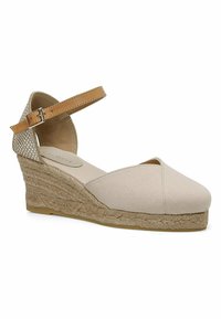 Beige canvas wedge sandaal met open teen, kruislings ontwerp en enkelbandje. De kurkachtige geweven zool voegt hoogte en textuur toe.