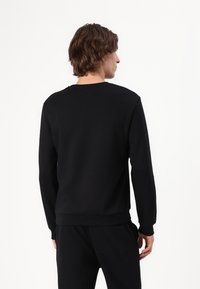 Melnas crew-neck džemperis ar garām piedurknēm, ribotām piedurknēm un apakšmalu, izgatavots no gludas auduma, ar regulāru piegriezumu un bez redzamas zīmola identifikācijas.