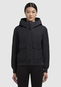 Veste à capuche noire avec fermeture éclair sur le devant, deux grandes poches avant et poignets côtelés. Texture lisse avec un subtil logo de la marque sur la poitrine.