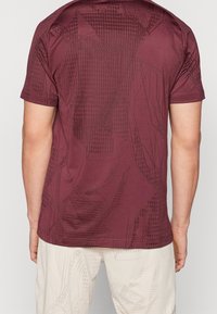 Kortärmad, vinröd t-shirt med ett geometriskt mönster och slät tygfinish samt rundad halsringning.