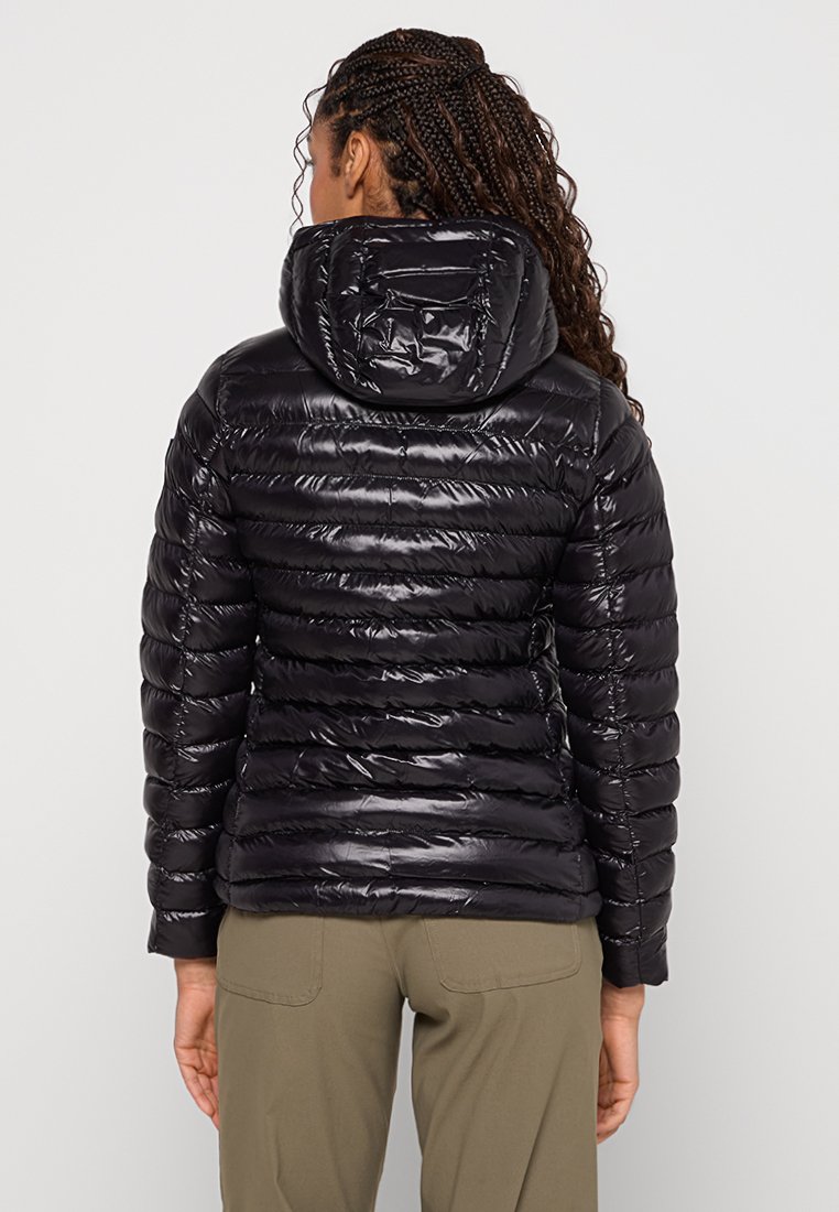 Czarna kurtka puchowa z błyszczącą, pikowaną teksturą, kapturem i detalami w prążki, widziana z tyłu, w połączeniu z khaki spodniami.