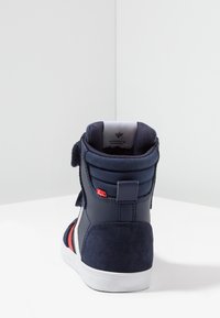 Zapatillas altas de color azul marino con parte superior de ante y sintético, suela de goma blanca, cierre de gancho y bucle, y acentos rojos.