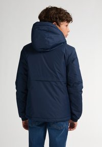 Marineblaue Kapuzenjacke mit einer strukturierten, wasserabweisenden Oberfläche. Mit einer schlanken Form und elastischen Bündchen, von hinten betrachtet.