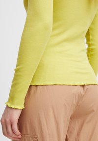 Rippenshirt mit langen Ärmeln in leuchtendem Gelb, mit ausgefranstem Saum und Manschetten, kombiniert mit hellbraunen Cargo-Hosen mit Seitentasche.