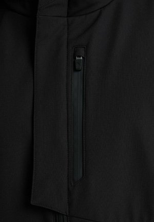 Približek navpičnega črnega zadrge na črnem oblačilu, ki prikazuje detajle zadrge in šivov.