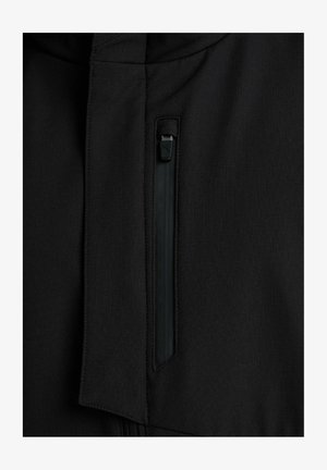 Prim-plan al unui fermoar vertical negru pe o țesătură neagră, arătând detaliile de trăgător al fermoarului și cusăturile.