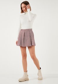 Maglione bianco a coste con collo alto, gonna a ruota rossa e bianca con fantasia, e stivaletti beige con suola spessa, mostrati in una posa in piedi.