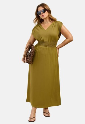 Kobieta ubrana w oliwkową suknię maxi z marszczoną talią, czarne okulary przeciwsłoneczne, trzyma brązową plecioną kopertówkę i ma na sobie czarne sandały na białym tle.