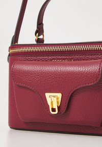 Burgundy textured leather handbag with gold zipper, front flap pocket, and gold clasp, handheld strap visible on top.